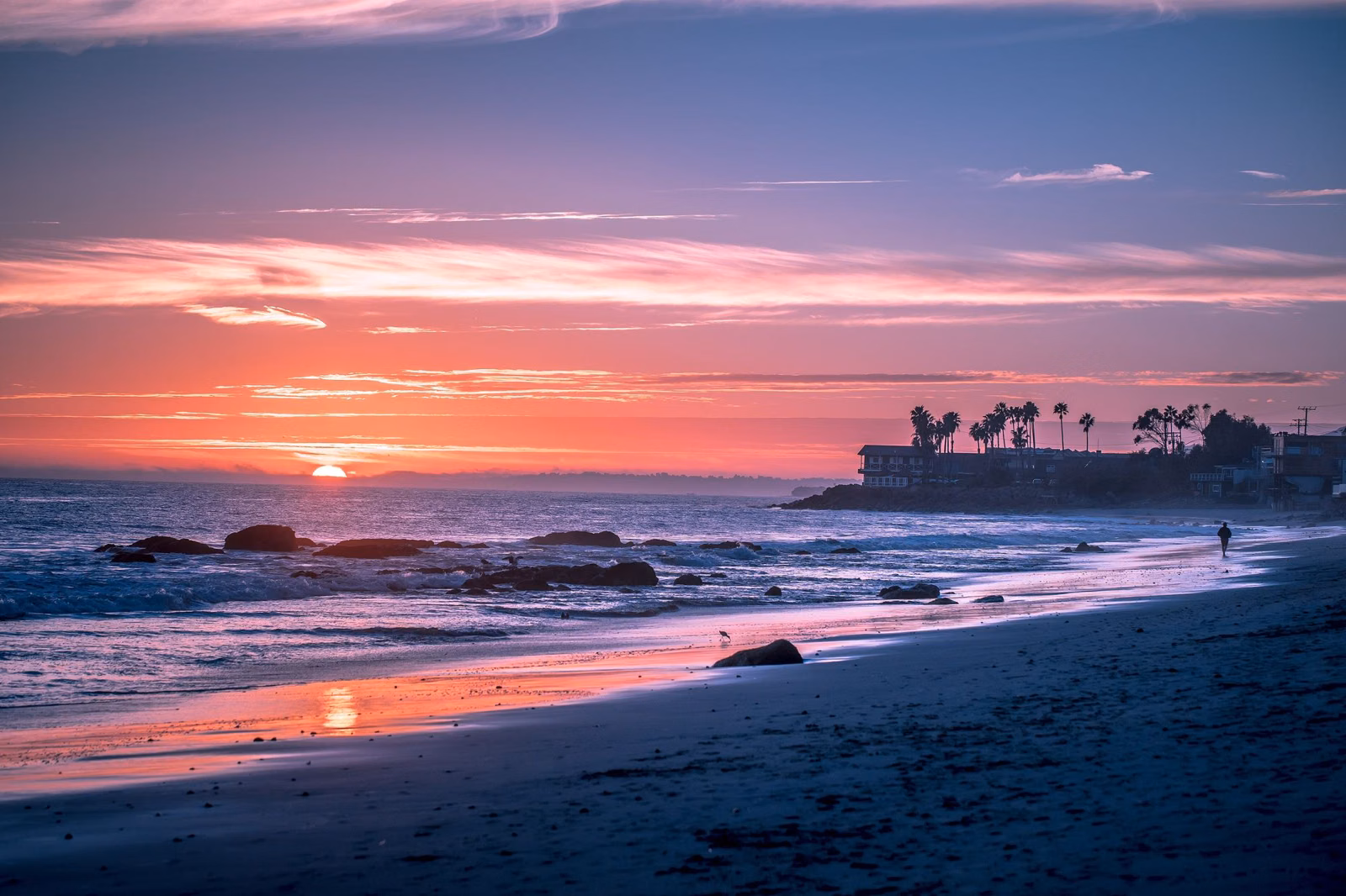 Sunset over the Pacific from a Malibu beach, with palm trees on the point and rocks in the surf